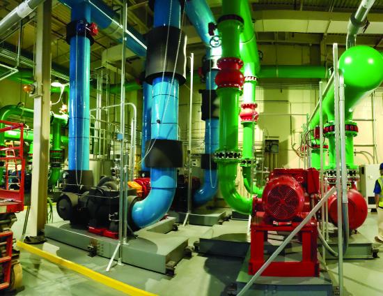 Photo of an industrial mechanical room with large blue and green insulated pipes, and red pump motors mounted on equipment pads.